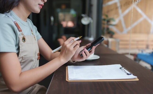 Asian,Barista,Taking,Orders,And,Managing,Inventory,Using,A,Smartphone