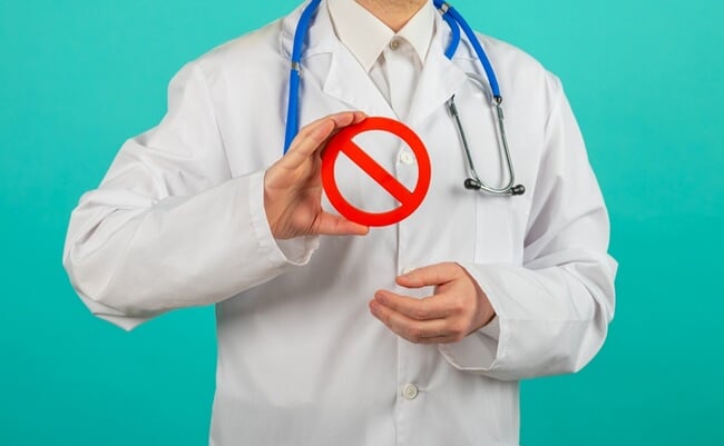 Male,Doctor,Holding,Prohibited,Sign,Over,Blue,Background