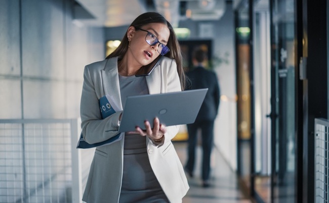 Businesswoman,Walks,Through,A,Modern,Office,Hallway,While,Talking,On