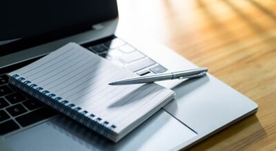 Laptop,Computer,With,Pen,And,Spiral,Notebook,On,Desk