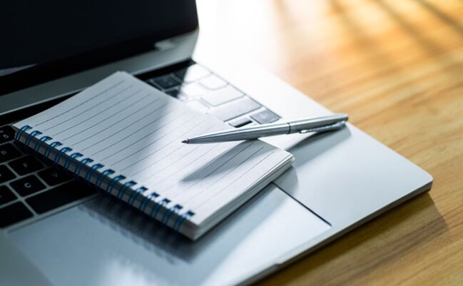 Laptop,Computer,With,Pen,And,Spiral,Notebook,On,Desk