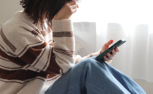 Depressed,Woman,Sitting,On,Bed,Looking,At,Smartphone,And,Crying